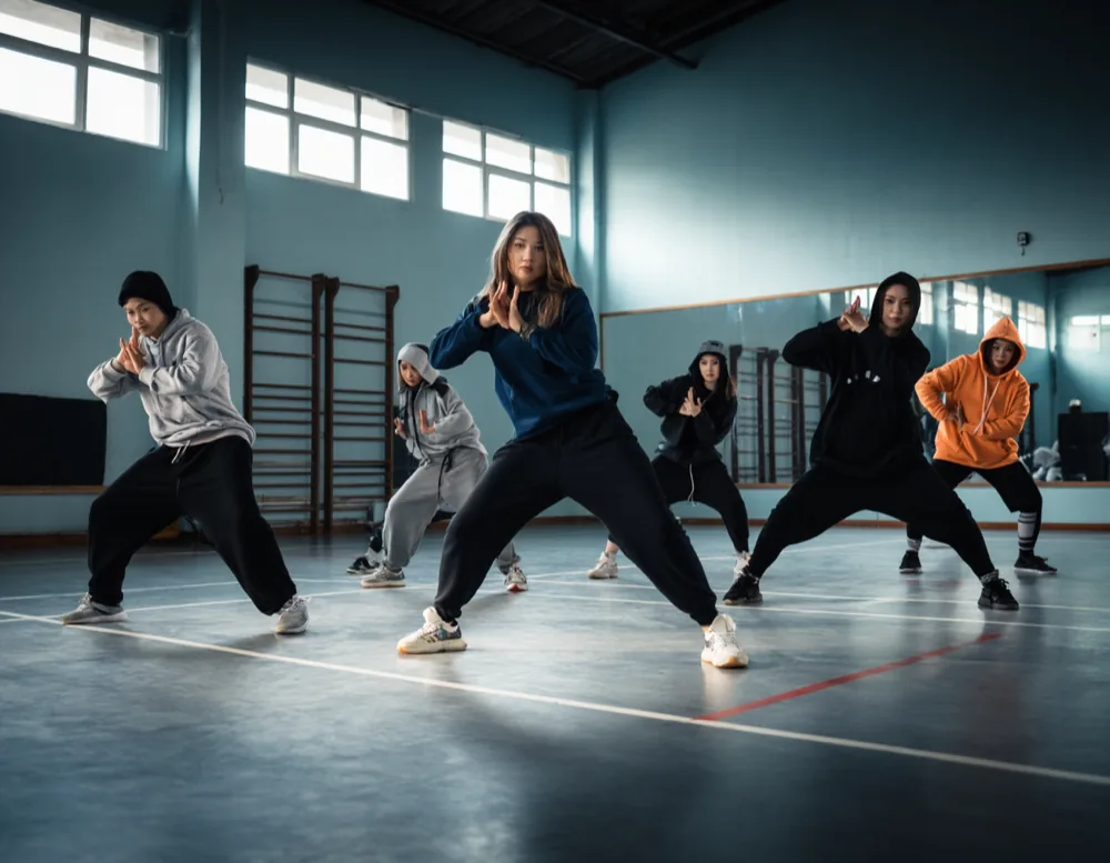 Hip hop class in the converted gymnasium, eight dancers in a wide stance
