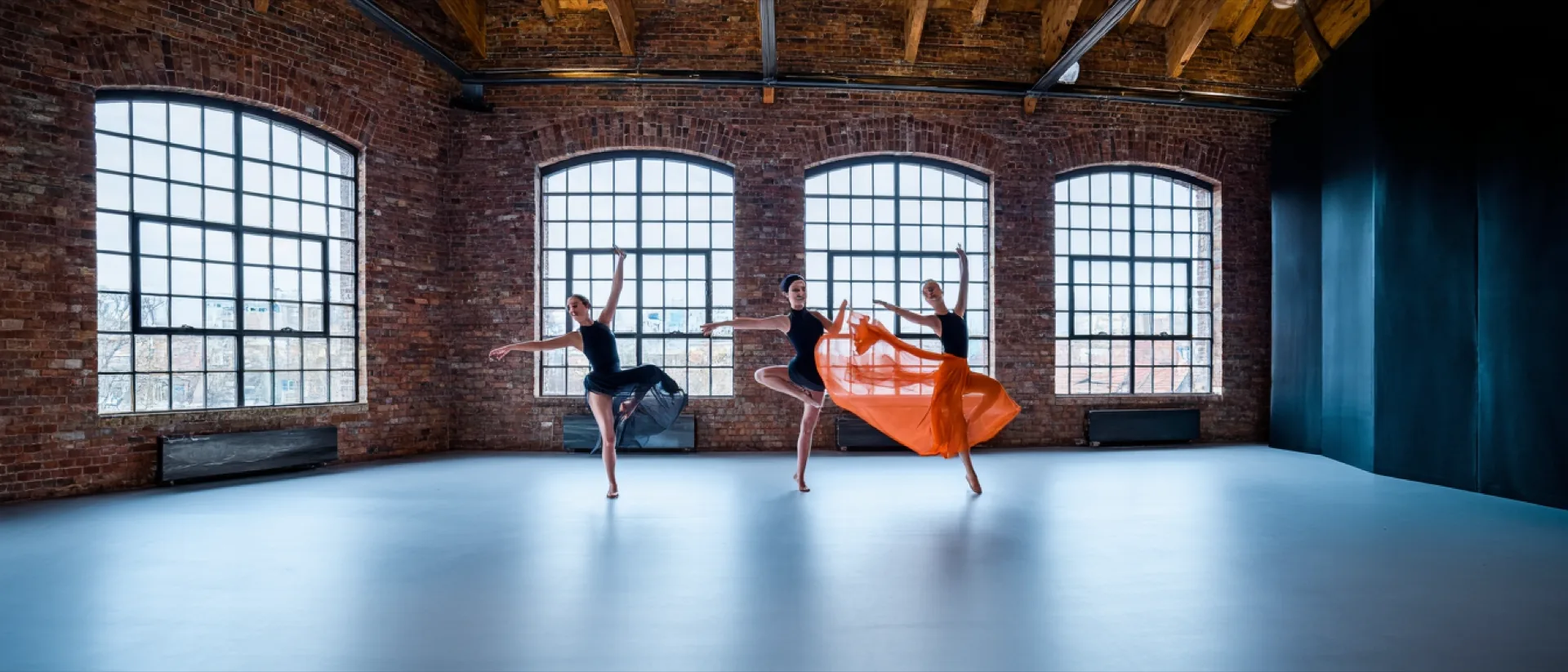 Three dancers mid-phrase in the loft studio in Hohenfelde, tall arched factory windows behind them