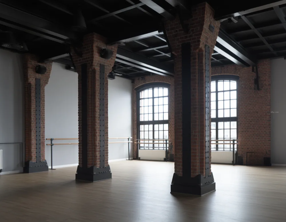 Empty loft dance studio with brick pillars, oak floor and tall factory windows
